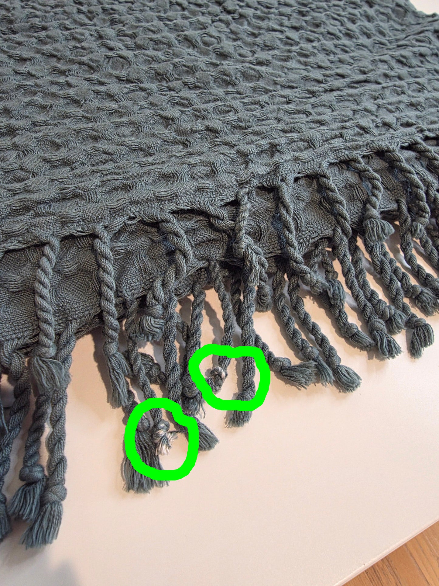 folded teal colored textured blanket with tassels - inperfections circled in green