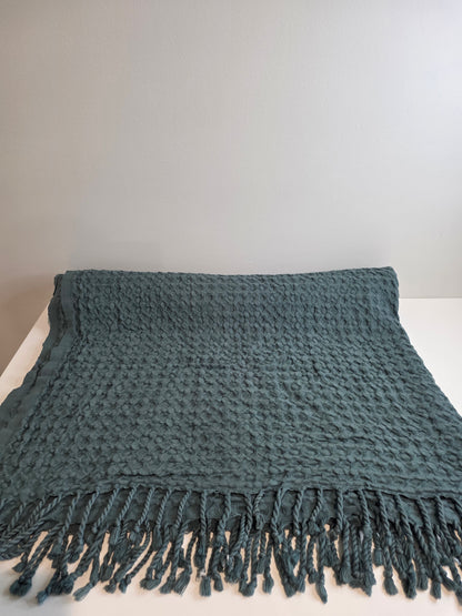 folded teal colored textured blanket with tassels