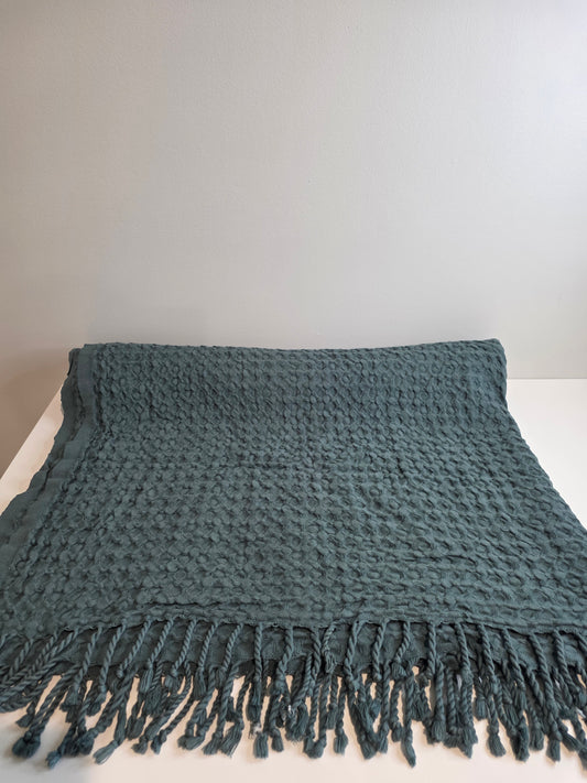 folded teal colored textured blanket with tassels
