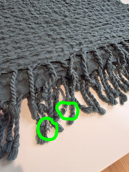 folded teal colored textured blanket with tassels - inperfections circled in green
