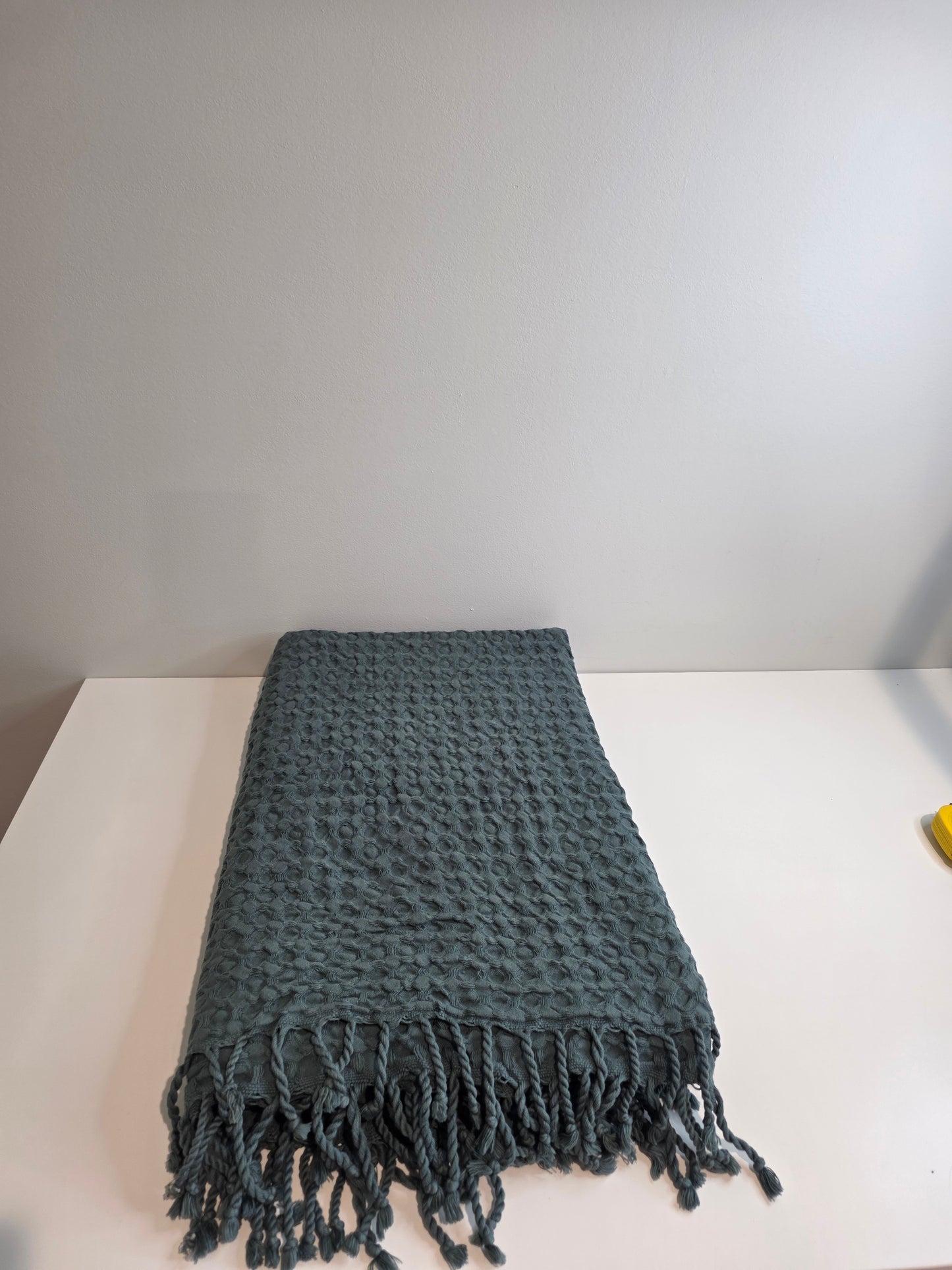 folded teal colored textured blanket with tassels