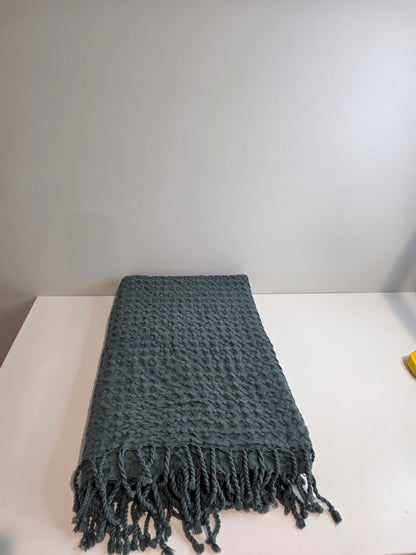 folded teal colored textured blanket with tassels