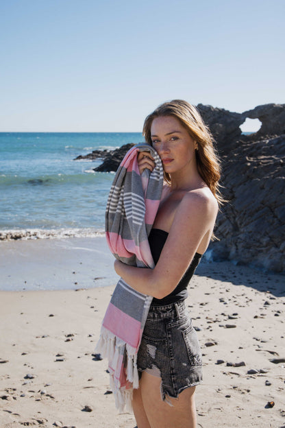 Woman holding a striped towel on a beach with ocean and rocks in the background