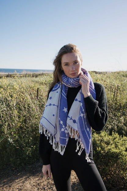 Woman wearing a blue and white patterned towel as a scarf outdoors with greenery and a clear sky.