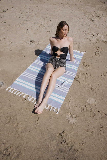 Woman sitting on a striped beach towel in the sand