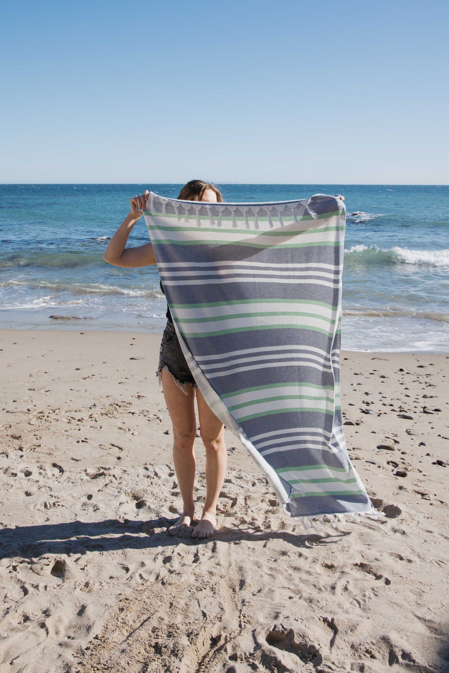 Person holding a striped towel on a beach with ocean in the background