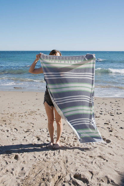 Person holding a striped towel on a beach with ocean in the background