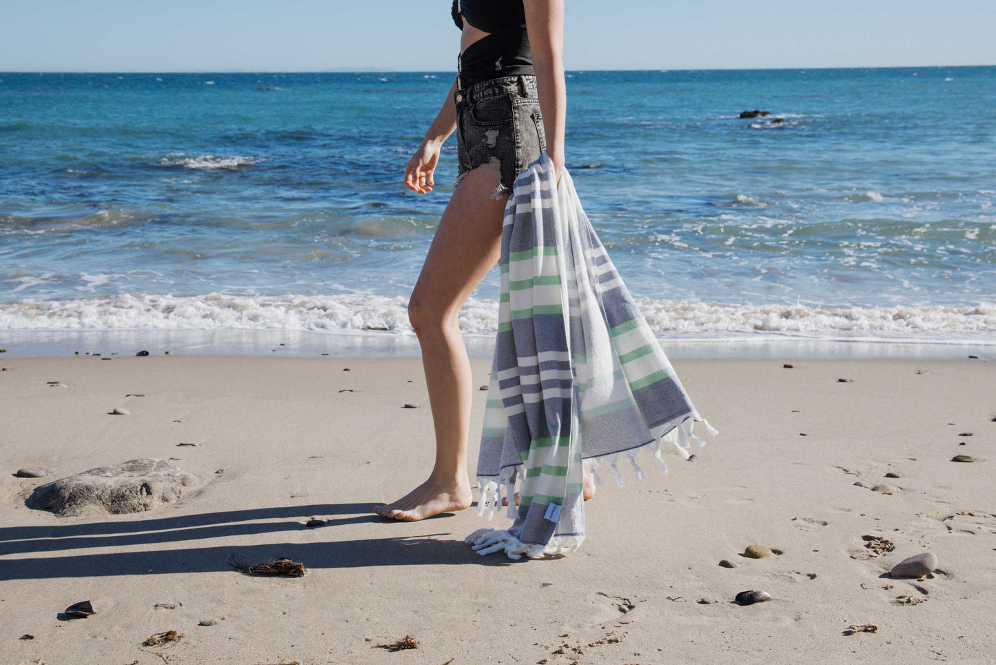 Person standing on a beach with a blue striped towel and ocean waves in the background