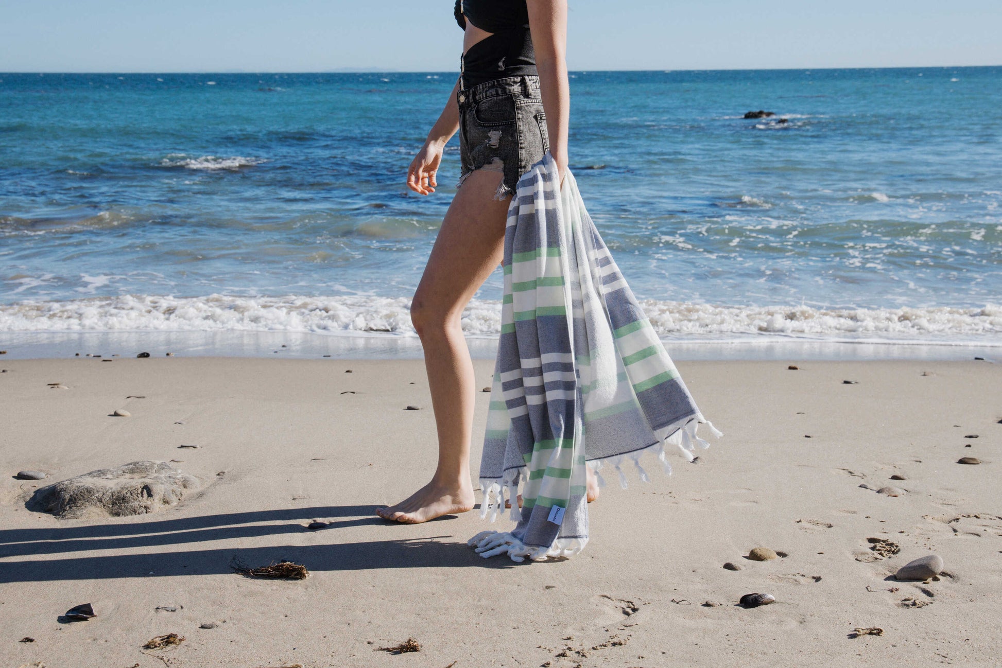 Person standing on a beach with a blue striped towel and ocean waves in the background