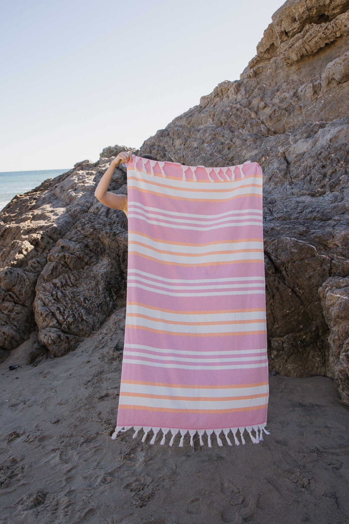 Person holding a pink striped towel on a rocky beach