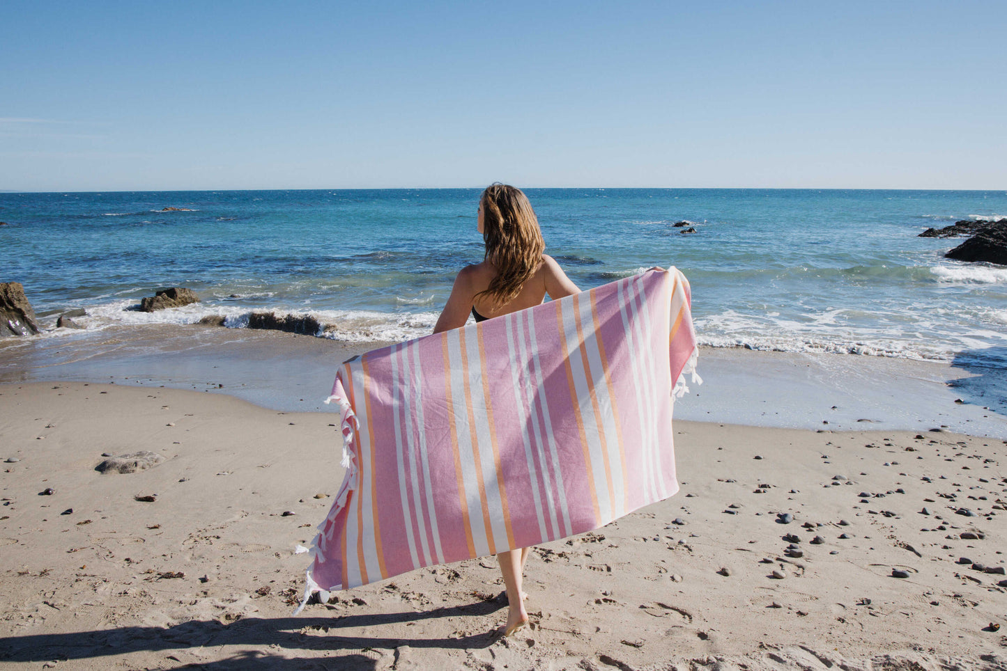 Woman holding a striped towel on a beach with ocean view