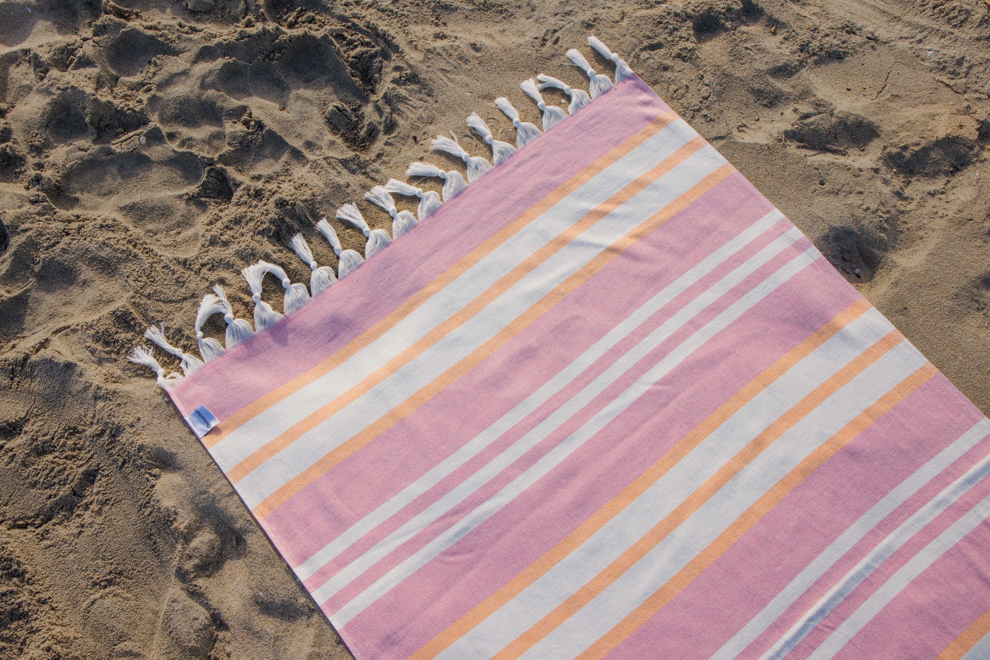 Striped beach towel with tassels on a sandy surface