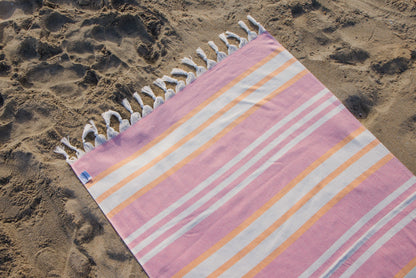Striped beach towel with tassels on a sandy surface