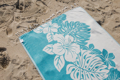 Turquoise beach towel with white floral patterns on sand