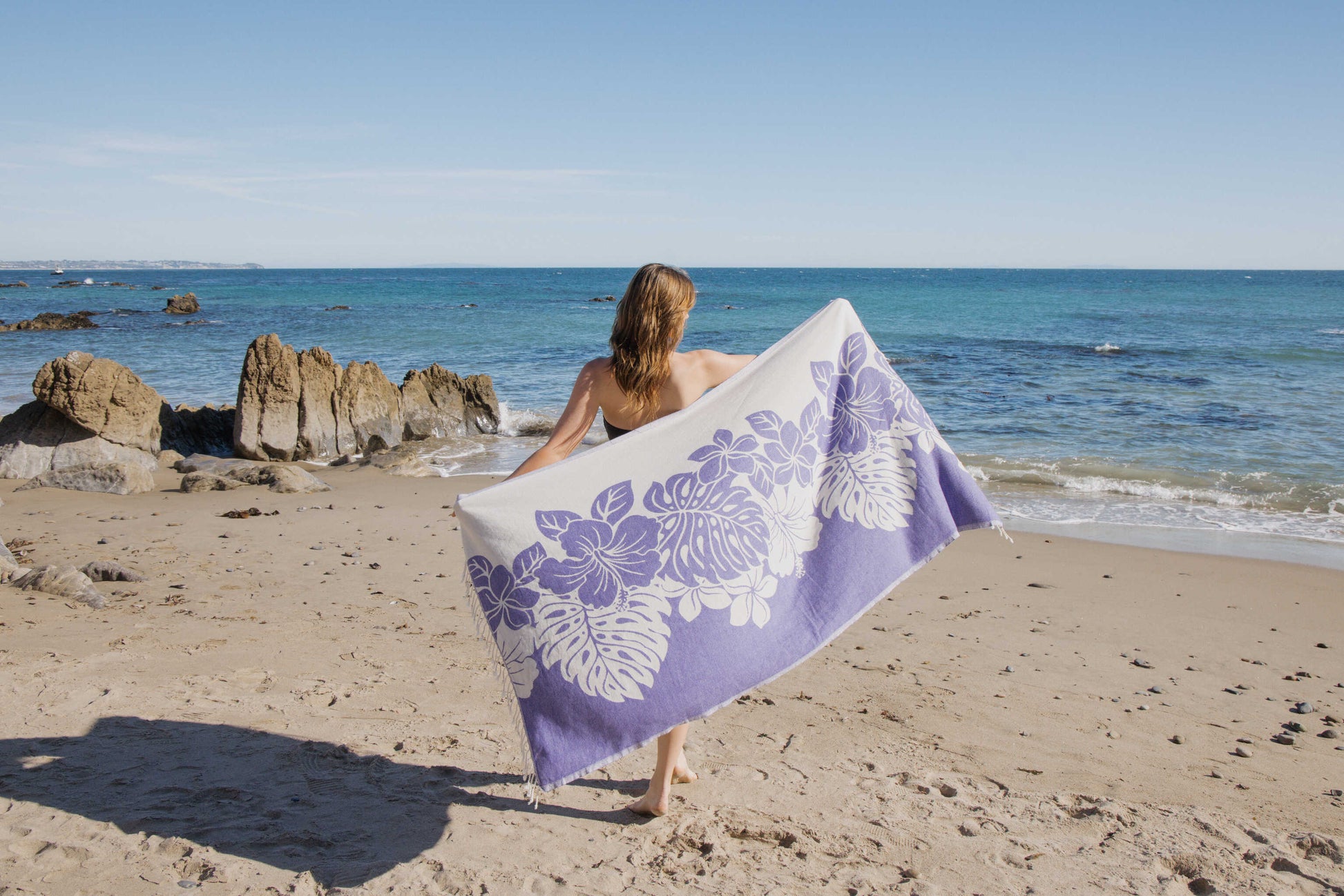 Person holding a purple and white floral towel on a beach