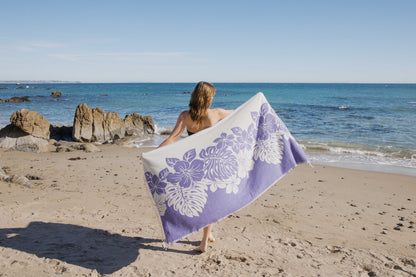 Person holding a purple and white floral towel on a beach