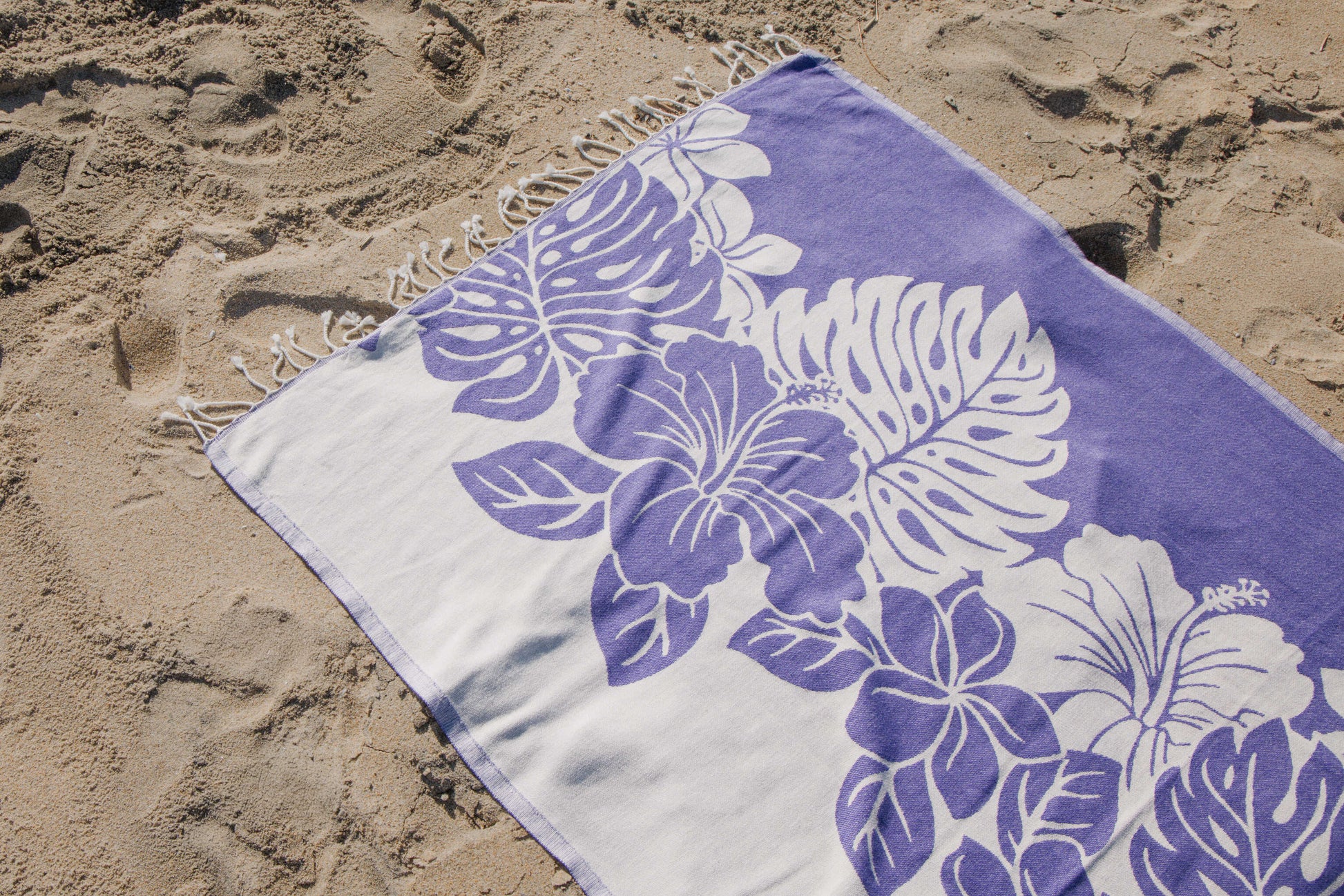 Beach towel with purple floral design on sand