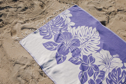 Beach towel with purple floral design on sand