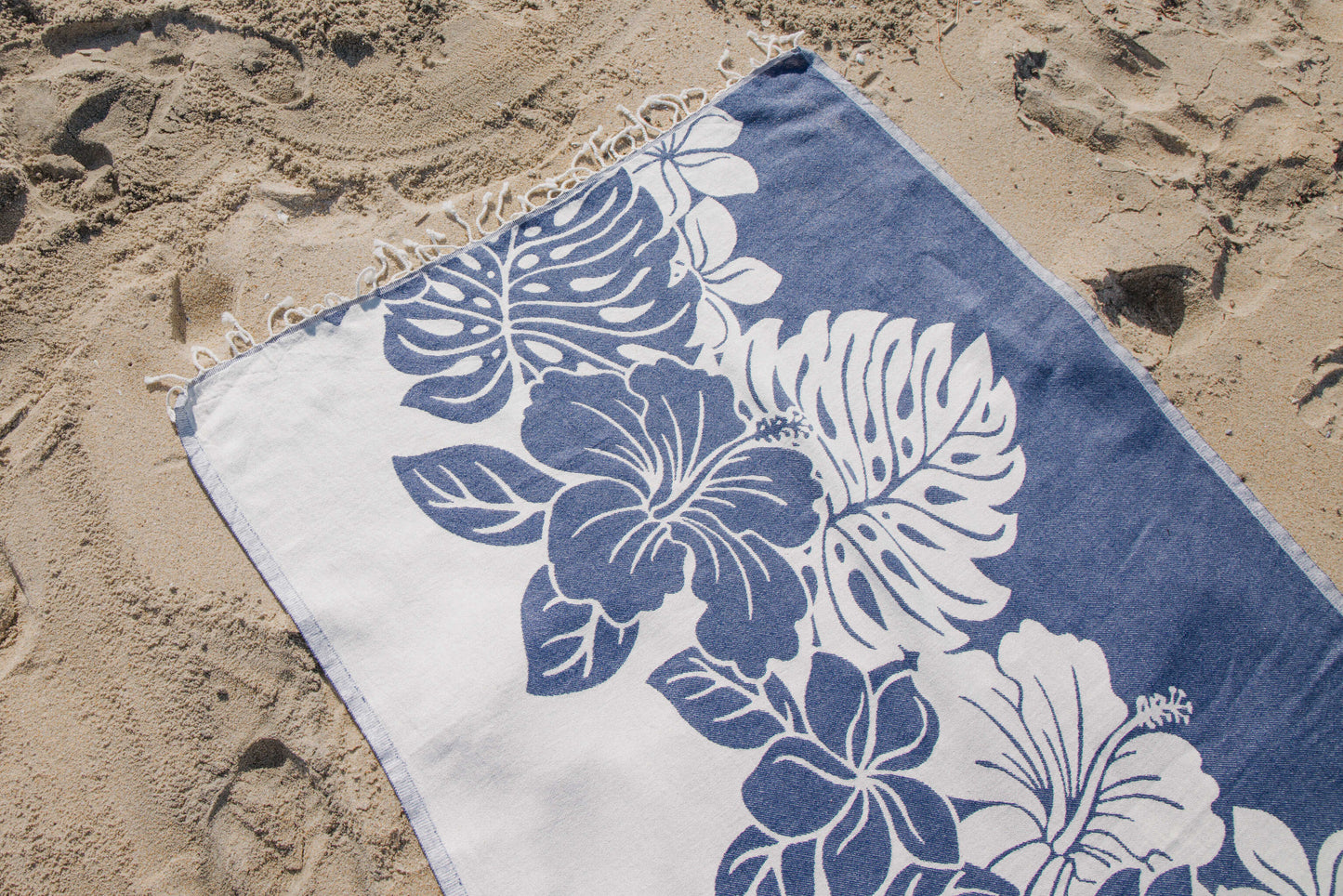 Blue and white floral towel on sandy beach