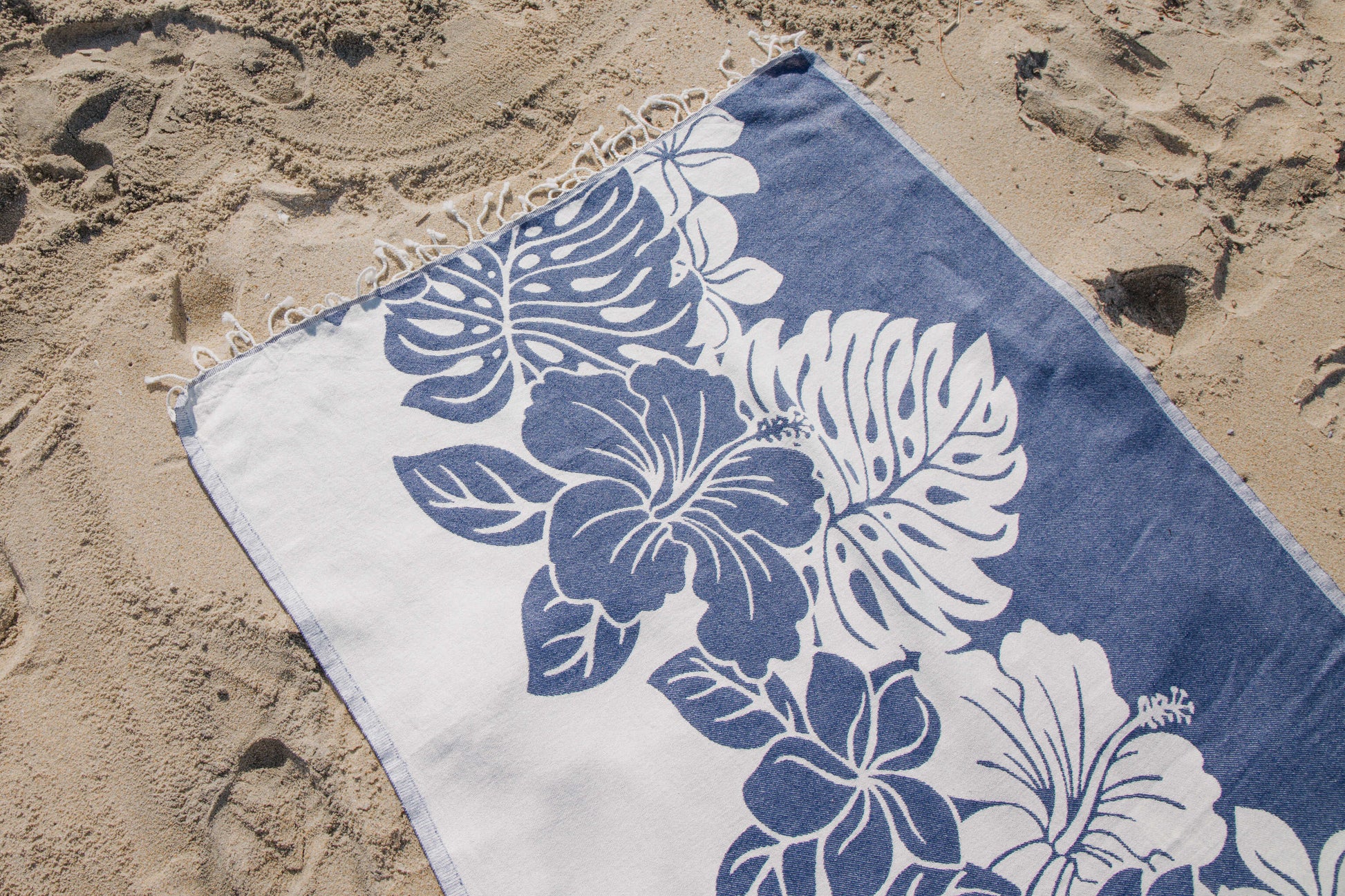 Blue and white floral towel on sandy beach