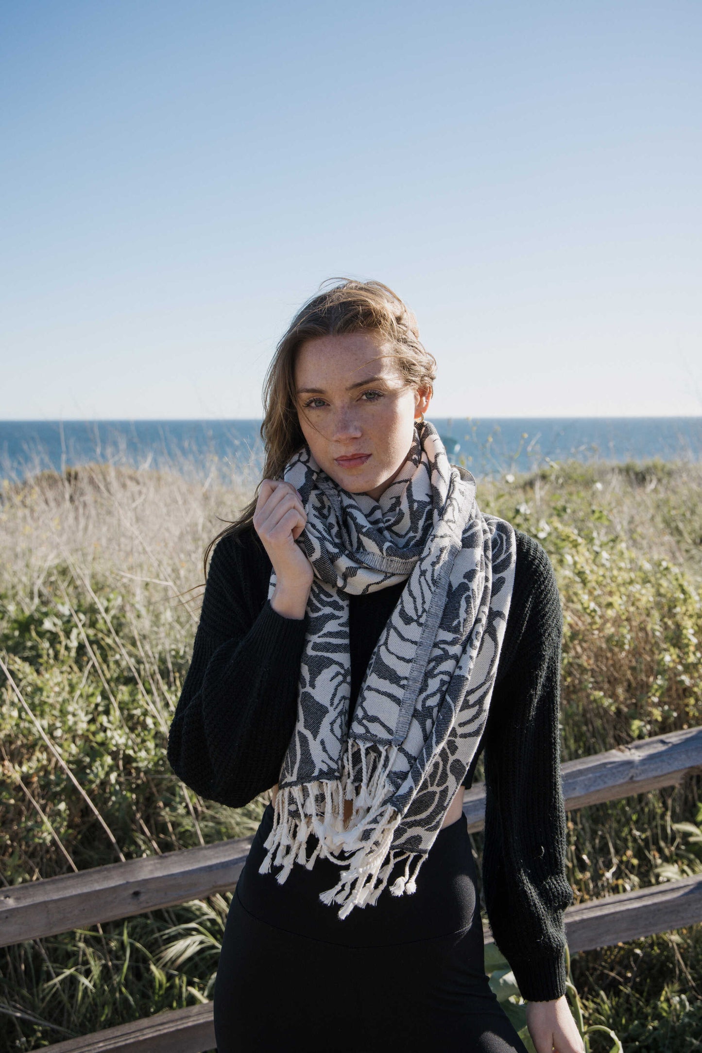 Woman wearing a rose patterned towel as a scarf, standing on a beach with ocean in the background