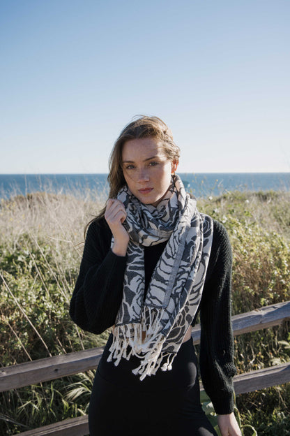 Woman wearing a rose patterned towel as a scarf, standing on a beach with ocean in the background