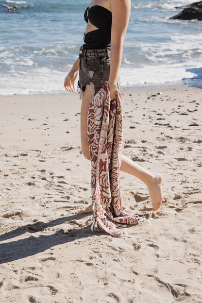 Person on a beach with a rose patterned towel in one hand