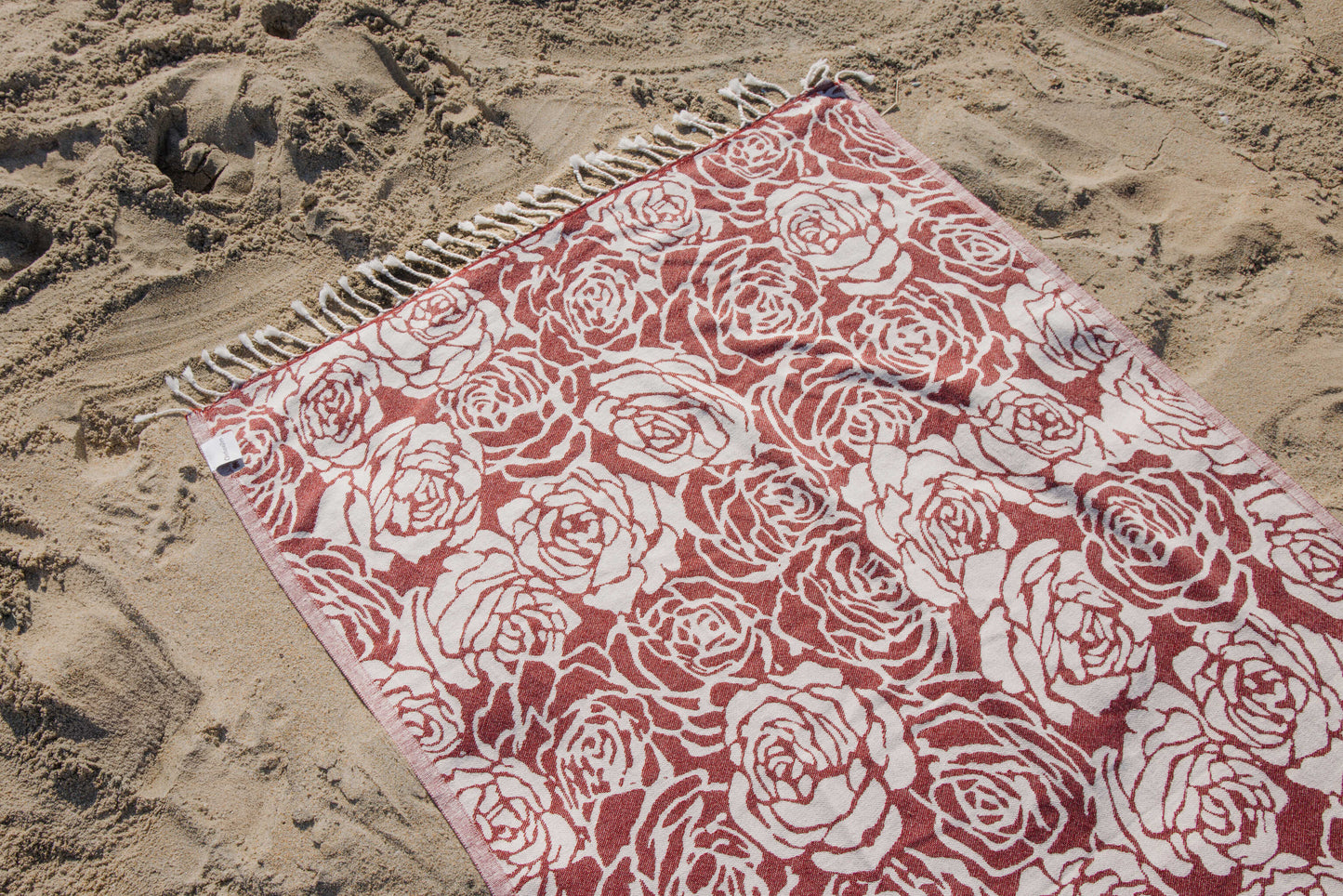 Red and white floral patterned towel on a sandy beach