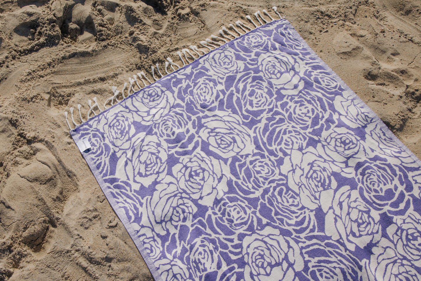 purple rose towel laying on the sand on a beach