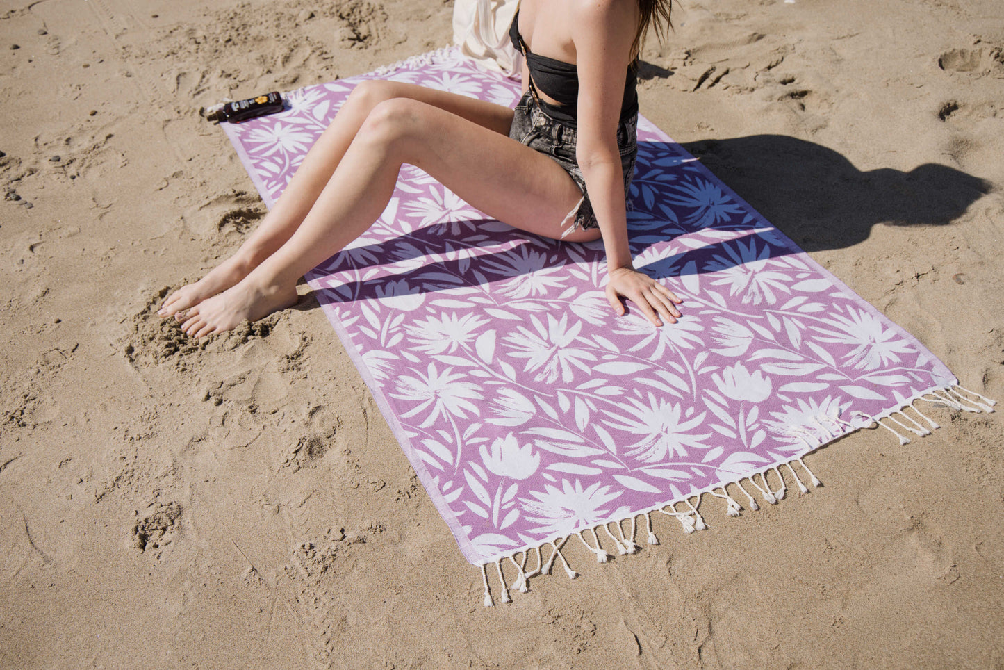 Person sitting on a purple floral beach towel in the sand